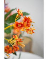 Närbild av den 108 cm artificiella grenen Daphne Spray i livfull orange, med realistiska gröna blad och gula ståndare, mot en mjukt blek bakgrund.