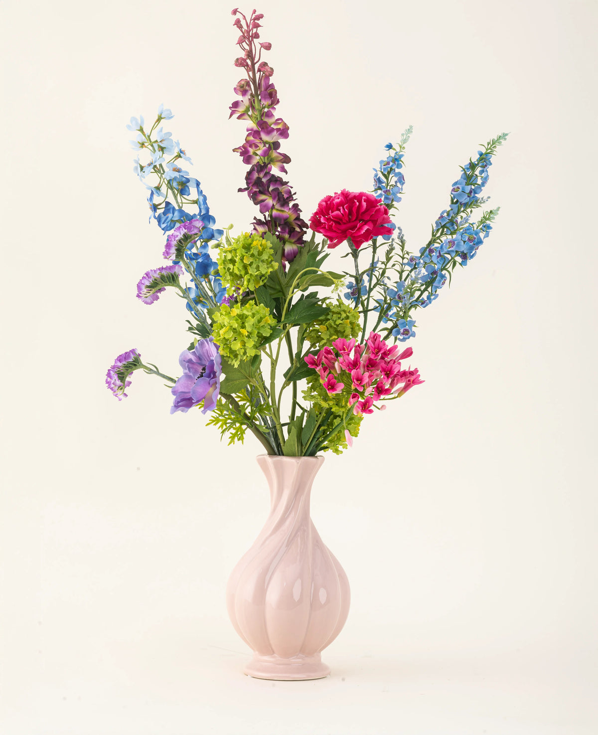 Arrangerad i en rosa keramisk vas, Blossom Breeze konstgjorda sidenblommabuketten har levande blÄ, lila, röda och gröna blommor - en underhÄllsfri blombukett mot en vanlig ljus bakgrund.