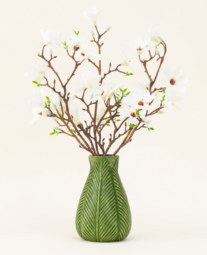 En grön vas visar Silk konstgjorda blombuketten Magnolia white, med flera vita magnoliakrenar med små gröna blad, mot en vanlig ljus bakgrund.