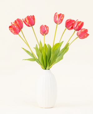 Sidens konstgjorda blombukett French Tulip red är arrangerad i en vit keramikvas, med åtta röda och gula tulpaner med gröna blad mot en vanlig ljus bakgrund.