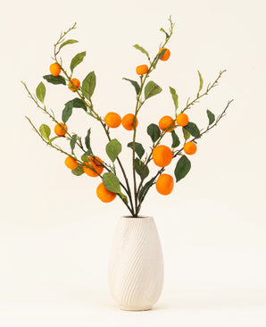 Silk konstgjorda blombuketten Mandarin har en vit texturerad vas och grenar av gröna löv och livfulla orange konstgjorda mandariner, som ger en livlig touch mot en vanlig ljus bakgrund.