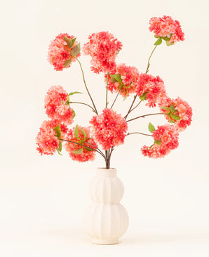 Silk Artificial Flowers Bouquet Cherry Blossom Coral har levande rosa och korall konstgjorda körsbärsblommor med gröna blad, elegant arrangerade i en vit skulpterad vas mot en ljus bakgrund.