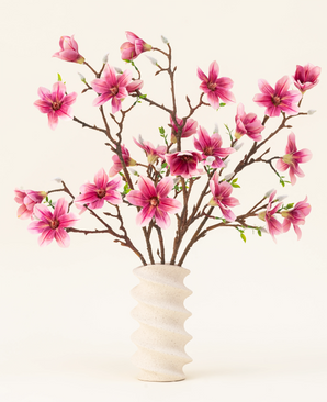 Silk konstgjorda blombuketten Magnolia rosa är arrangerad i en vågig vit keramikvas med gröna knoppar, vilket skapar en elegant skärm mot en ljus bakgrund.