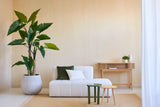 Ett minimalistiskt vardagsrum med växten Artificial Calocasia 210 cm, en vit texturerad soffa med gröna och vita kuddar, två små sidobord, en beige matta och ett konsolbord i trä mot en ljusbeige vägg.