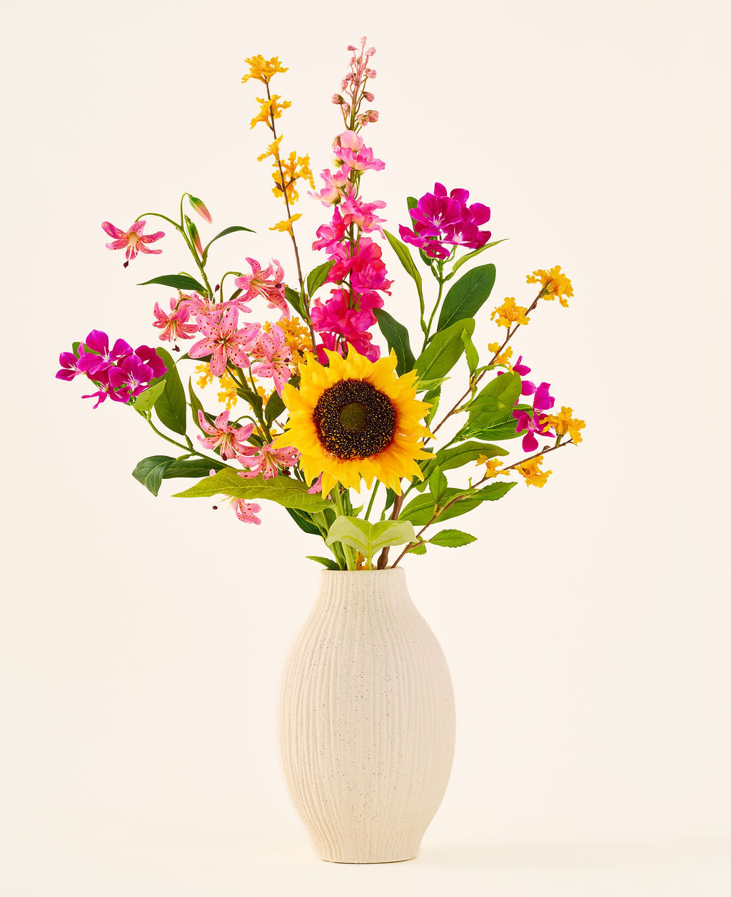 Sidens konstgjorda blombukett 'Tiny Sunshine' placeras i en beige keramikvas, bestående av en konstgjord bukett av verklighetstrogna blommor, såsom en stor solros, rosa och magentablommor och gula blommor med gröna blad, mot en vanlig ljus bakgrund. Detta arrangemang från Easyplants består av vackra sidenblommor som lägger till långvarig skönhet till alla rum.