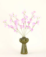 En grön glasvas visar Silk konstgjorda blombuketten Pea rosa med mjukt grönt bladverk, med flera långa stjälkar och mot en vanlig benvit bakgrund.