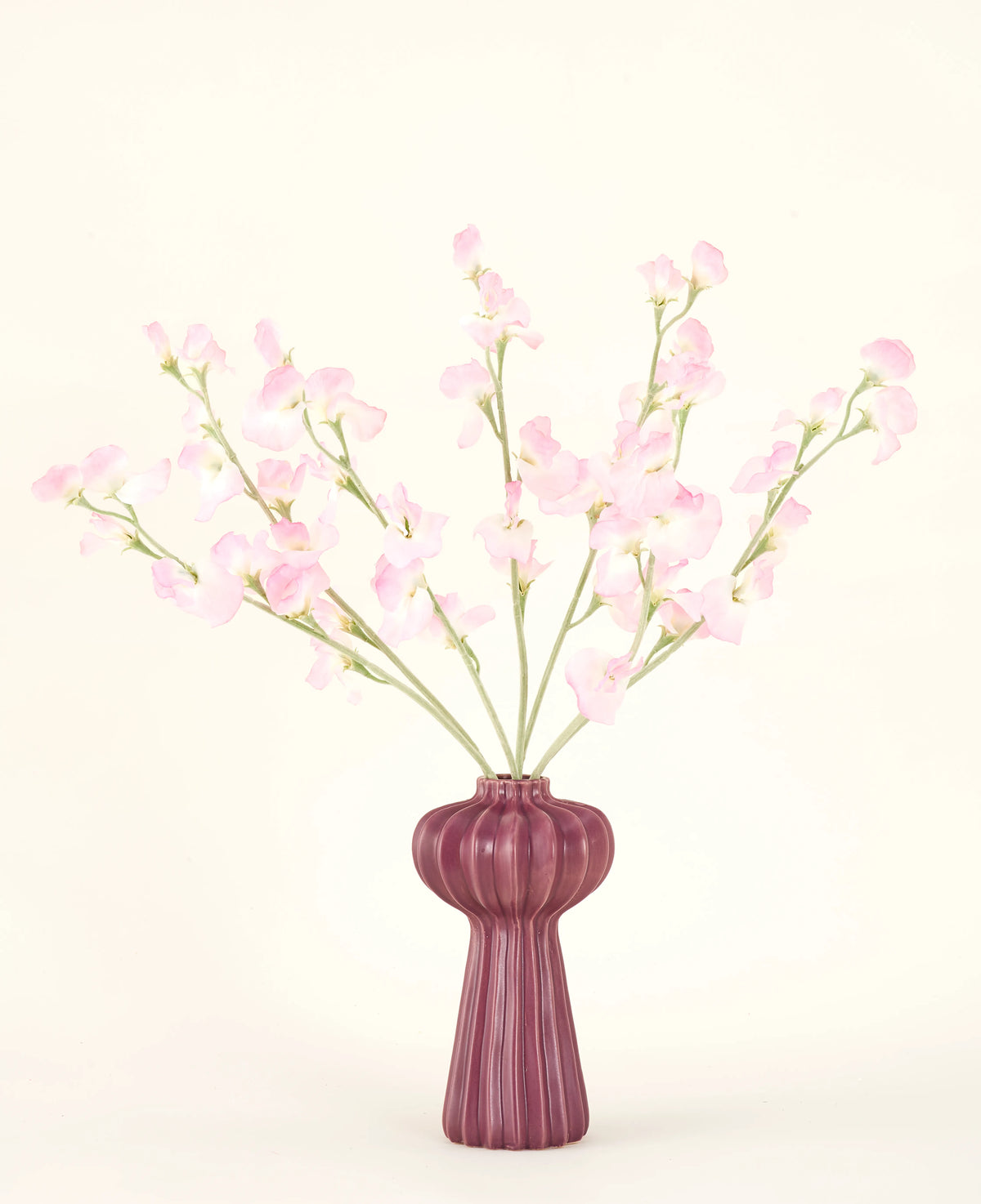 Silk konstgjorda blombuketten Pea ljusrosa, med flera ljusrosa ärtstjälkar i en räfflad vinröd vas, står mot en blek bakgrund - perfekt för alla konstgjorda blommor interiör.