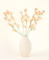 Den krämfärgade keramikvasen innehåller Silk konstgjorda blombuketten Pea Peach, med delikat persika och ljusrosa blommor med långa gröna stjälkar mot en ljus, neutral bakgrund.