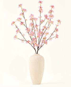 En hög beige keramikvas innehåller flera grenar från Silk konstgjorda blombuketten Rosa blommor, med fina rosa blommor och gröna blad, mot en vanlig vit bakgrund.
