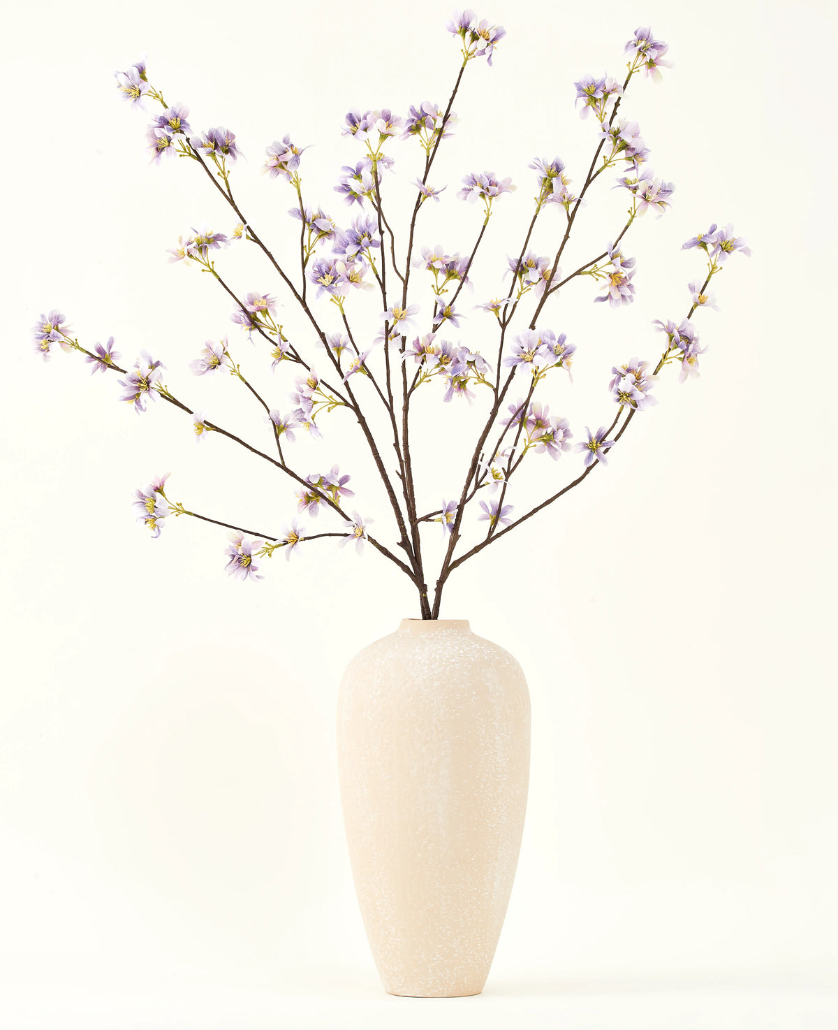 En hög, krämfärgad keramikvas innehåller ett antal tunna grenar med texten Silk konstgjord blombukett Konstgjord blomgren lila, mot en slät, ljus bakgrund.