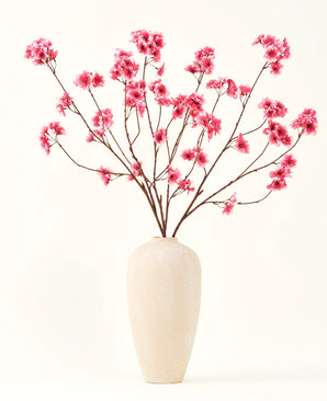 Silk konstgjorda blombuketten Cherry blossom fuchsia 114 cm tillför en livlig färg till din interiör med sina slående grenar och fuchsiablommor, vackert utställda i en beige keramikvas mot en vanlig benvit bakgrund.