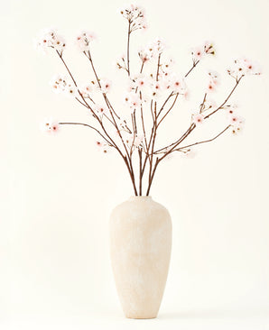 Silk konstgjorda blombuketten Cherry blossom rouge 114 cm har höga, känsliga grenar i en enkel beige vas, som ger en mjuk, elegant touch till din inredning mot en enkel, ljus bakgrund.
