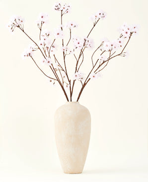 Sidens konstgjorda blombukett Körsbärsblommor ljusrosa 114 cm står i en hög beige keramikvas med långa, tunna grenar och delikata ljusrosa blommor, vilket skapar en fridfull konstgjord blommig accent mot en enkel bakgrund.