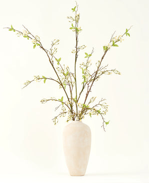 En hög, krämfärgad keramikvas innehåller Silk konstgjorda blombuketten Verbena kräm med långa grenar, små gröna blad och fina vita blommor, vackert arrangerade mot en vanlig ljus bakgrund.
