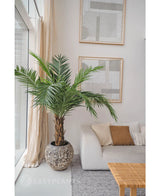 Artificiell Palm Phoenix Canarie 160 cm tillför en tropisk atmosfär bredvid en ljus soffa med neutrala kuddar i ett modernt vardagsrum med abstrakt konst, transparenta gardiner och ett vävt soffbord.