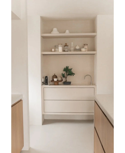 Minimalistisk kökshörna med ljusa trähyllor med krukor, vaser, dekor, bänkskiva med små vitvaror och krukväxten Artificiell Bonsai Juniper 40 cm, plus inbyggda lådor och en liten kran - allt i neutrala toner.