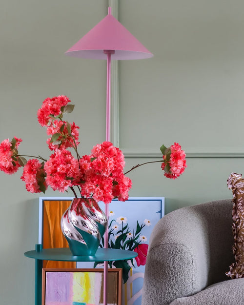 En rosa lampa, en randig vas med Silk Artificial Flower Bouquet Cherry Blossom Coral, färgglada konstverk och en grå stol står mot en ljusgrön vägg och skapar en mysig, livlig hörna.