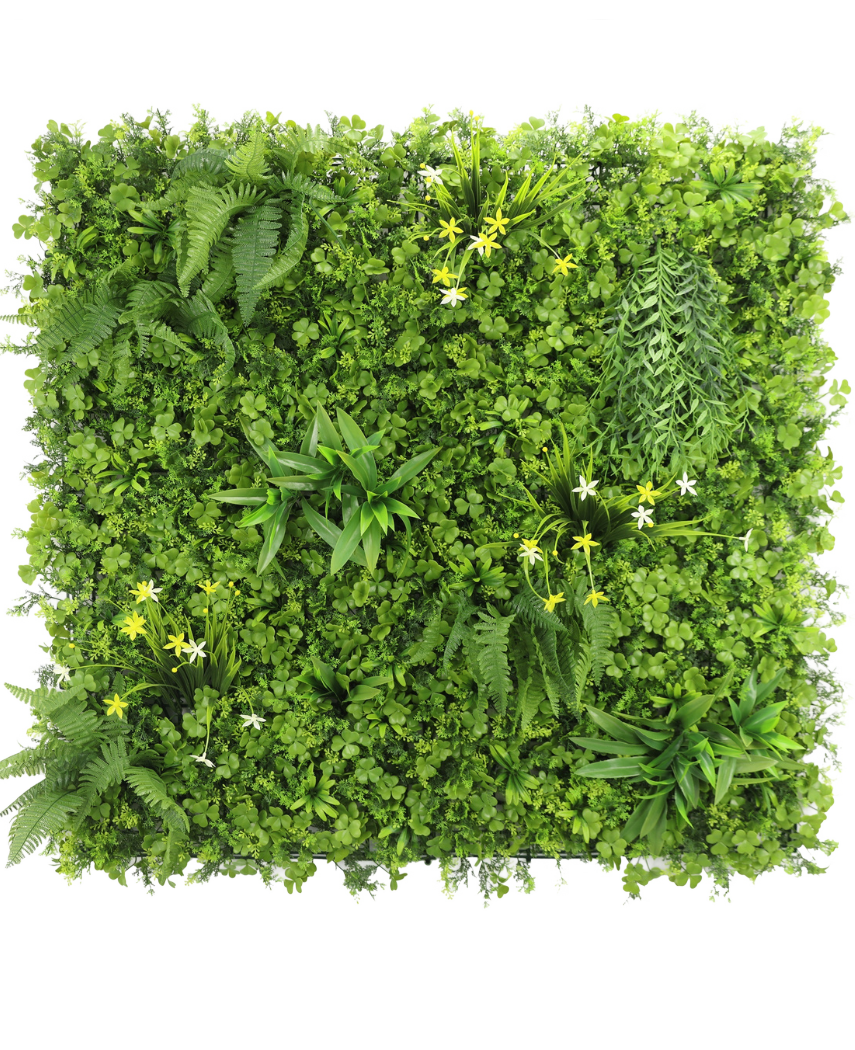 The Artificiell Hedge Daffodil Smile 100x100 cm UV är en fyrkantig vertikal grön vägg med tätt grönt bladverk, ormbunkar och små gula och vita blommor, mot en vit bakgrund sett från ovan.