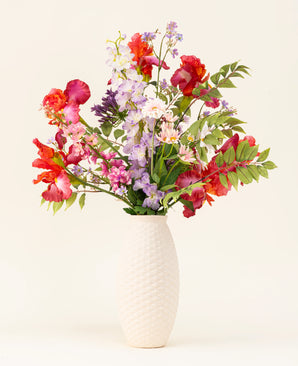 In een vaas met witte structuur staat het Zijden kunstbloemen boeket Pink Pop, met levendige kunstroze bloemen en groene bladeren tegen een lichte achtergrond.