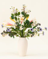 In een witte vaas staat het Zijden kunstbloemen boeket Blush & Bloom - met roze lelies, witte en paarse bloemen en weelderige groene bladeren - tegen een lichte achtergrond.