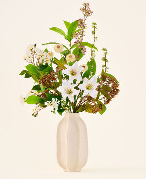 Siden konstgjord blombukett Timeless Bloom, bestående av en bukett av olika vita liljor, små vita blommor och grönska i en beige vas med struktur.