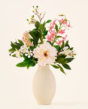 I en krämfärgad keramikvas ligger buketten 'Light & Lovely' med konstgjorda sidenblommor från Easyplants, bestående av ett blandat arrangemang av vita, rosa och ljuslila sidenblommor med gröna blad, mot en enkel, ljus bakgrund.