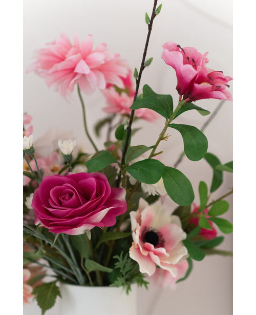 En närbild på Artificial Rose Real Touch 56 cm rosa, en bukett rosa konstgjorda rosor med gröna blad i en vit vas, mot en ljus bakgrund.