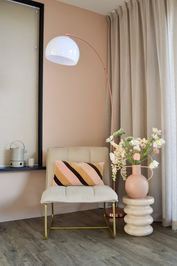 En modern, mysig hörna med en krämfärgad stol med randig kudde, en hög bågformad golvlampa, beiga gardiner, ett trägolv och en rund vas med Artificiell Blomma Fritillary 94 cm vita blommor på ett skulpterat sidobord.
