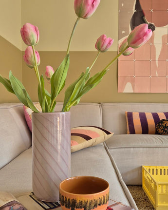 En 63 cm fransk konstgjord tulpan i rosa står i en vas på bordet bredvid en orange kopp i ett mysigt vardagsrum med en krämsoffa, mönstrade kuddar, en gul låda och abstrakt väggkonst i bakgrunden.