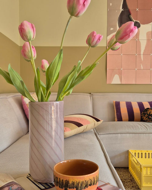 En 63 cm fransk konstgjord tulpan i rosa står i en vas på bordet bredvid en orange kopp i ett mysigt vardagsrum med en krämsoffa, mönstrade kuddar, en gul låda och abstrakt väggkonst i bakgrunden.