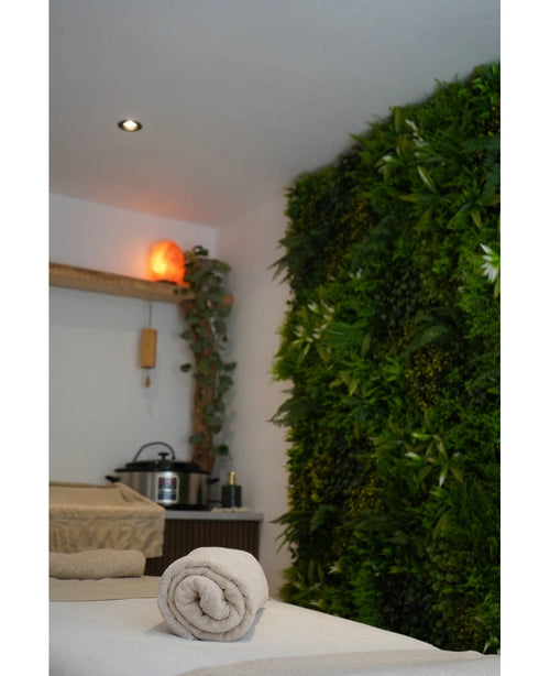 En lugn spaavdelning med massagebänk, lugnande belysning, en himalayasaltlampa på en hylla och en frodig Artificiell Hedge Freshness 100x100 cm UV-grön växtvägg för extra lugn.
