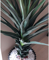 Een close-up van de Kunstplant Agave Pandora UV 120 cm, met groene stekelige bladeren in een zwarte pot met witte kiezels, uitgestald op een licht oppervlak tegen een neutrale muur.