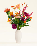 Een vaas met witte textuur bevat het Zijden kunstbloemen boeket Magnus di Lambo-roze, oranje, rode en paarse bloemen met groene bladeren-tegen een effen lichte achtergrond voor een levendige touch.