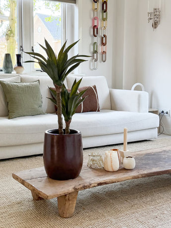 Ett modernt vardagsrum med en vit soffa, gröna och bruna kuddar, ett soffbord i trä dekorerat med ljus och den konstgjorda agaveplantan 76 cm, och en väggdekoration i kedjenät. Naturligt ljus kommer in genom fönstren bakom soffan.