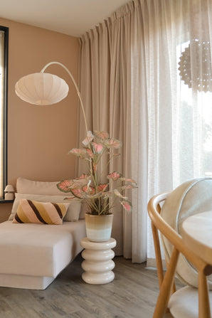 En mysig sittgrupp med en beige schäslong, en randig kudde, den Artificial Caladium 90 cm rosa som ger en touch av grönt, en modern lampa, ljusgardiner och ett trägolv. Mjukt naturligt ljus kommer in genom de genomskinliga gardinerna.