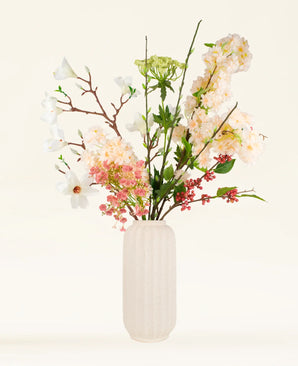 Het Zijden kunstbloemen boeket Springtime Poem, met witte en roze bloemen, groene bladeren en rode bessen in een witte vaas met textuur, wordt weergegeven tegen een lichte achtergrond.